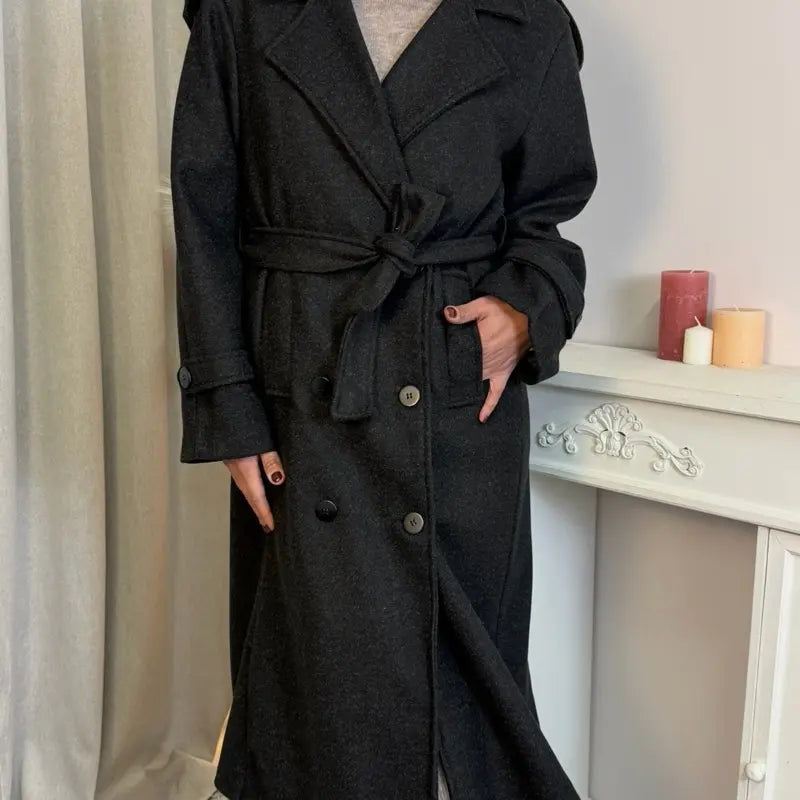 Ce manteau croisé présente une fermeture boutonnée, une ceinture intégrée et des poches pratiques, alliant élégance raffinée et praticité polyvalente.