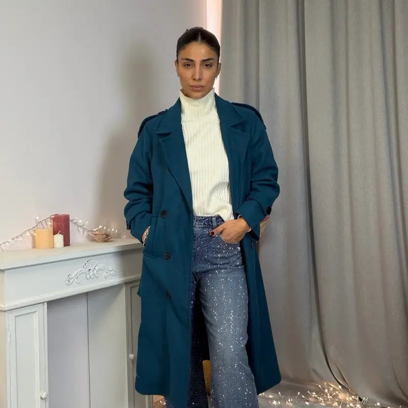 Ce manteau croisé présente une fermeture boutonnée, une ceinture intégrée et des poches pratiques, alliant élégance raffinée et praticité polyvalente.