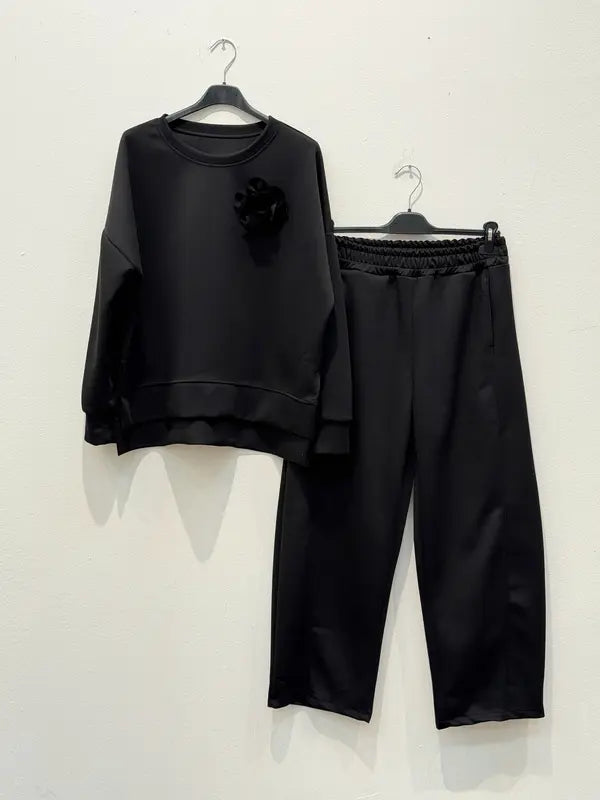 Cet ensemble de combinaison deux pièces, fabriqué en tissu viscose, comprend un haut orné d'une broche en forme de fleur et un pantalon sarouel élastiqué.